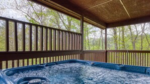 A hot tub with a wooden deck and railing, surrounded by trees.