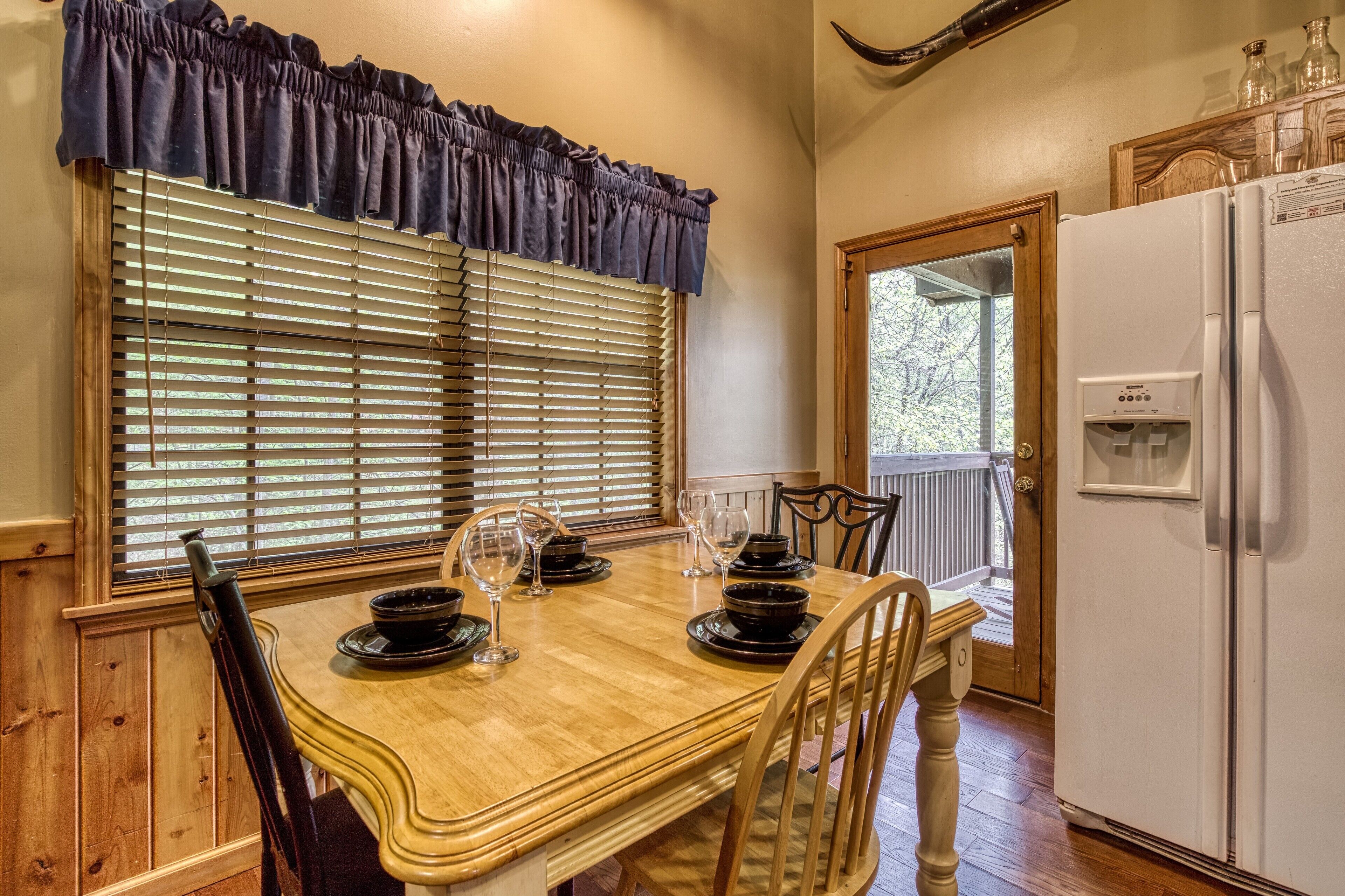 A dining table with chairs, a window with blinds, a refrigerator, and a door leading to an outdoor area.