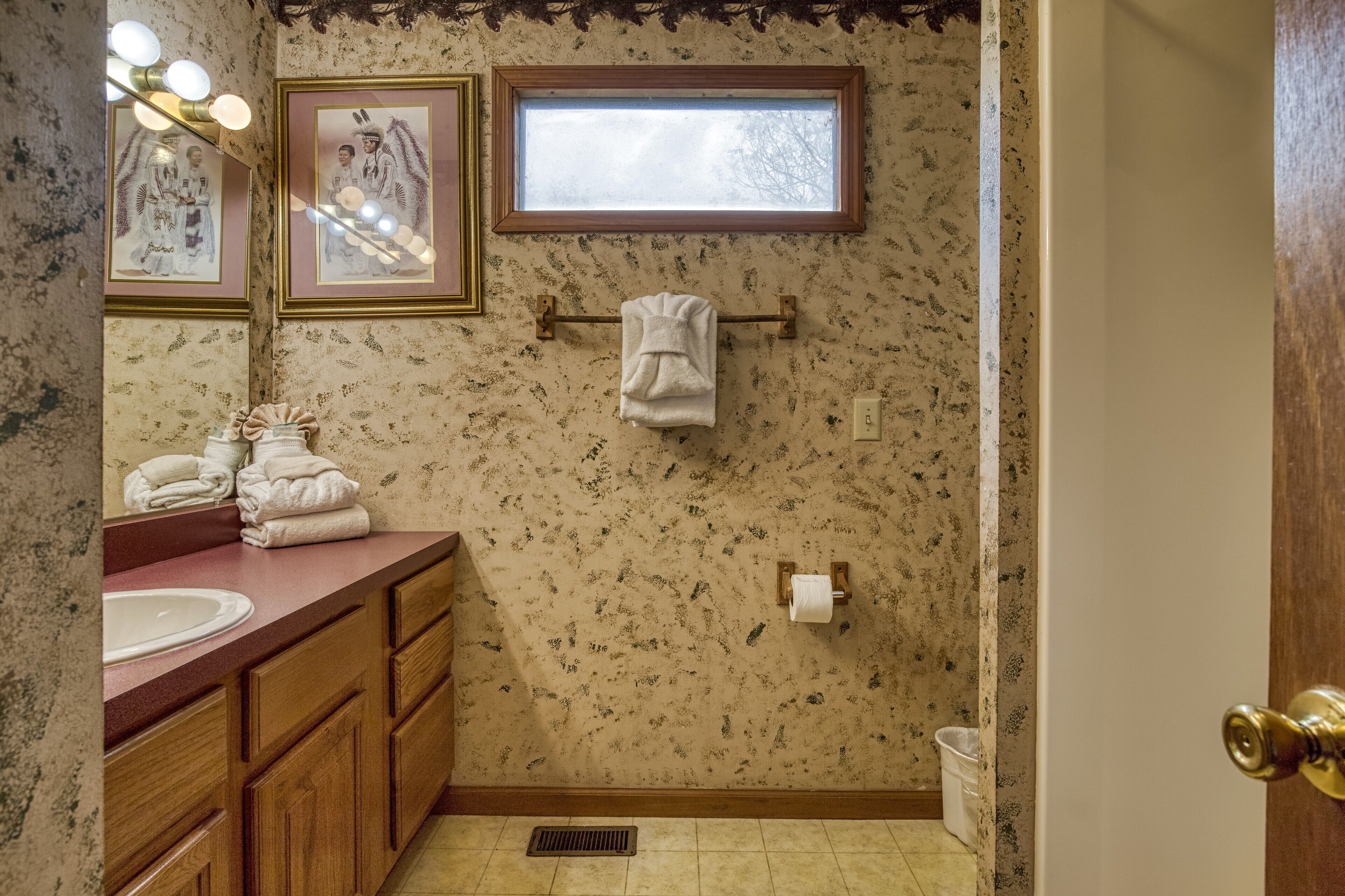 A bathroom with a sink, vanity, towel rack, and a window.