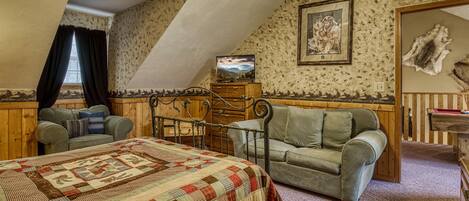 A cozy attic bedroom with a large bed, two sofas, a wooden dresser, and a television.