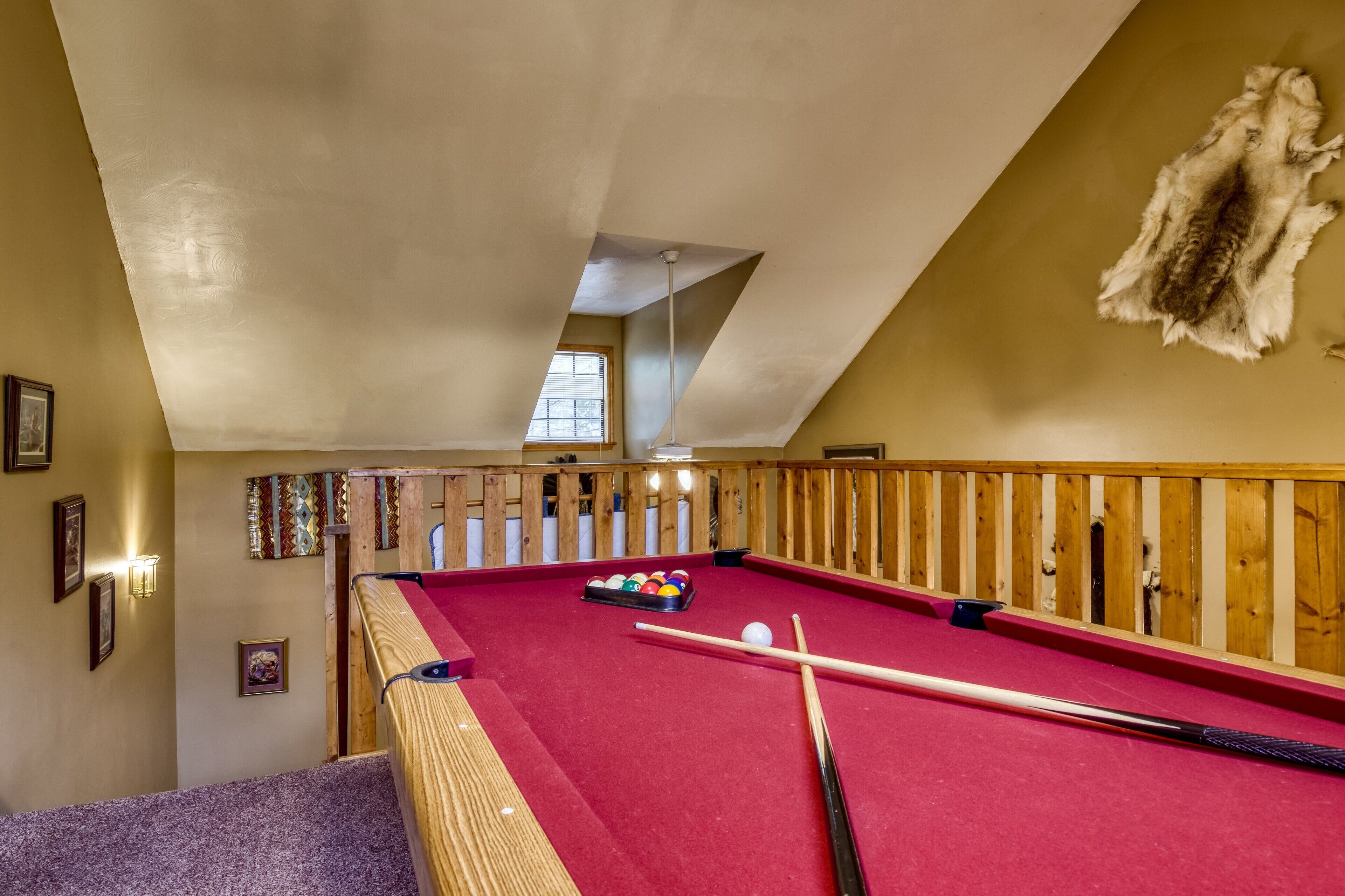 Een pooltafel in een ruimte met houten leuningen, ingelijste foto's aan de muur en een bont tapijt.