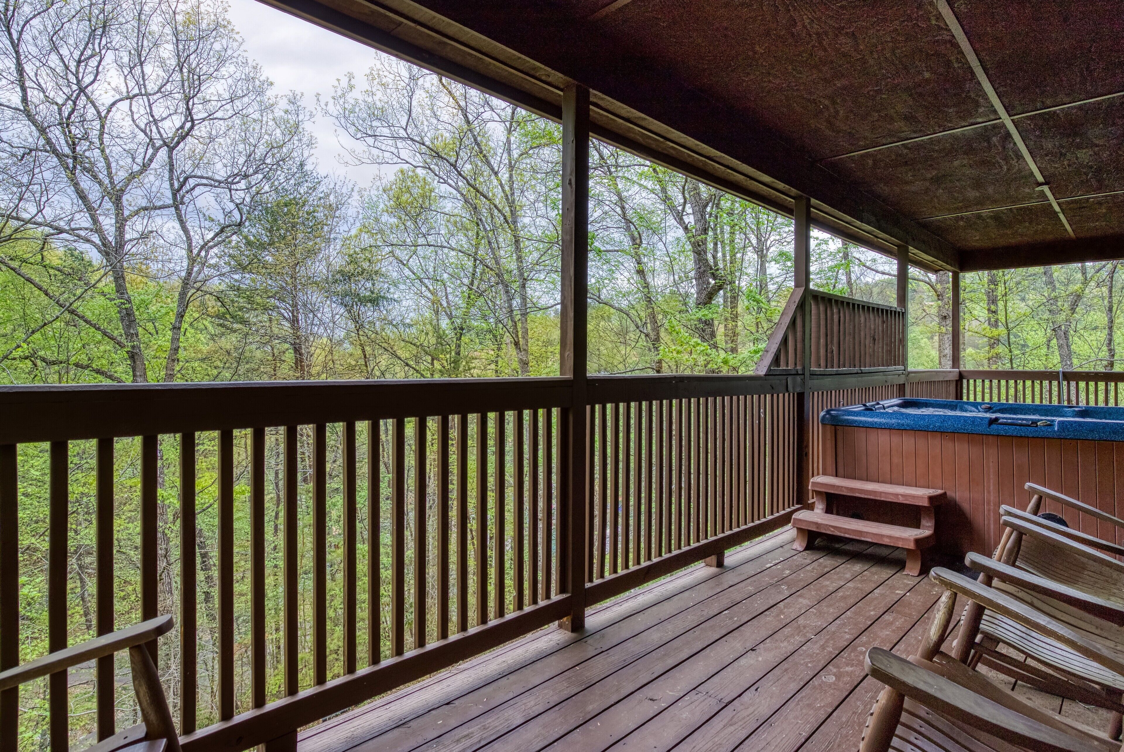 A wooden deck with a hot tub and benches, overlooking a forested area.