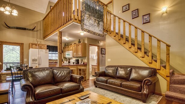 A spacious living area with two leather sofas, a wooden coffee table, and a staircase with wooden railings.