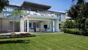 Une maison moderne dotée d’un espace extérieur aménagé avec un coin salon couvert, d’une pelouse bien entretenue et d’un grand arbre.