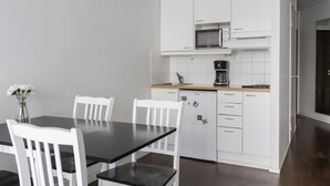 A modern kitchen with white cabinets, a microwave, and a coffee maker. There is a dining table with chairs and a vase of flowers. - 2ndhomes Kluuvi Apartments 2 (Helsinki)