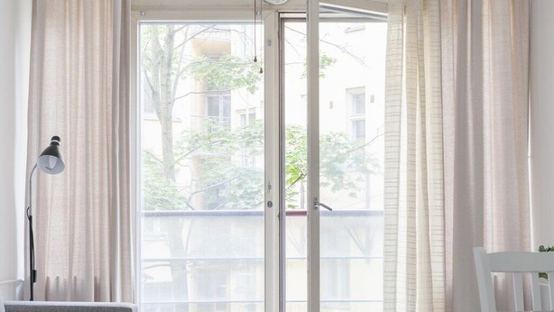 A room with a grey sofa, a white chair, a white rug, and a large sliding glass door with curtains. - 2ndhomes Kluuvi Apartments 2 (Helsinki)