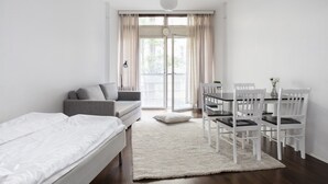A modern, minimalist bedroom with a bed, a sofa, a dining table with chairs, and a large window with curtains. - 2ndhomes Kluuvi Apartments 2 (Helsinki)
