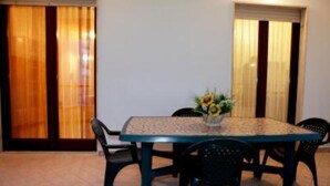A dining area with a table and chairs, a vase with flowers, and curtains on the windows. - Beachfront apartment in Residence Rosa Virginia Pool (Gallipoli)