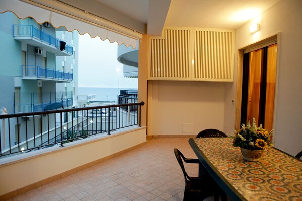 A balcony with a railing, a dining table with chairs, and a flower vase. - Beachfront apartment in Residence Rosa Virginia Pool (Gallipoli)
