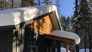 A wooden cabin with a covered porch and a snow-covered roof, surrounded by trees.