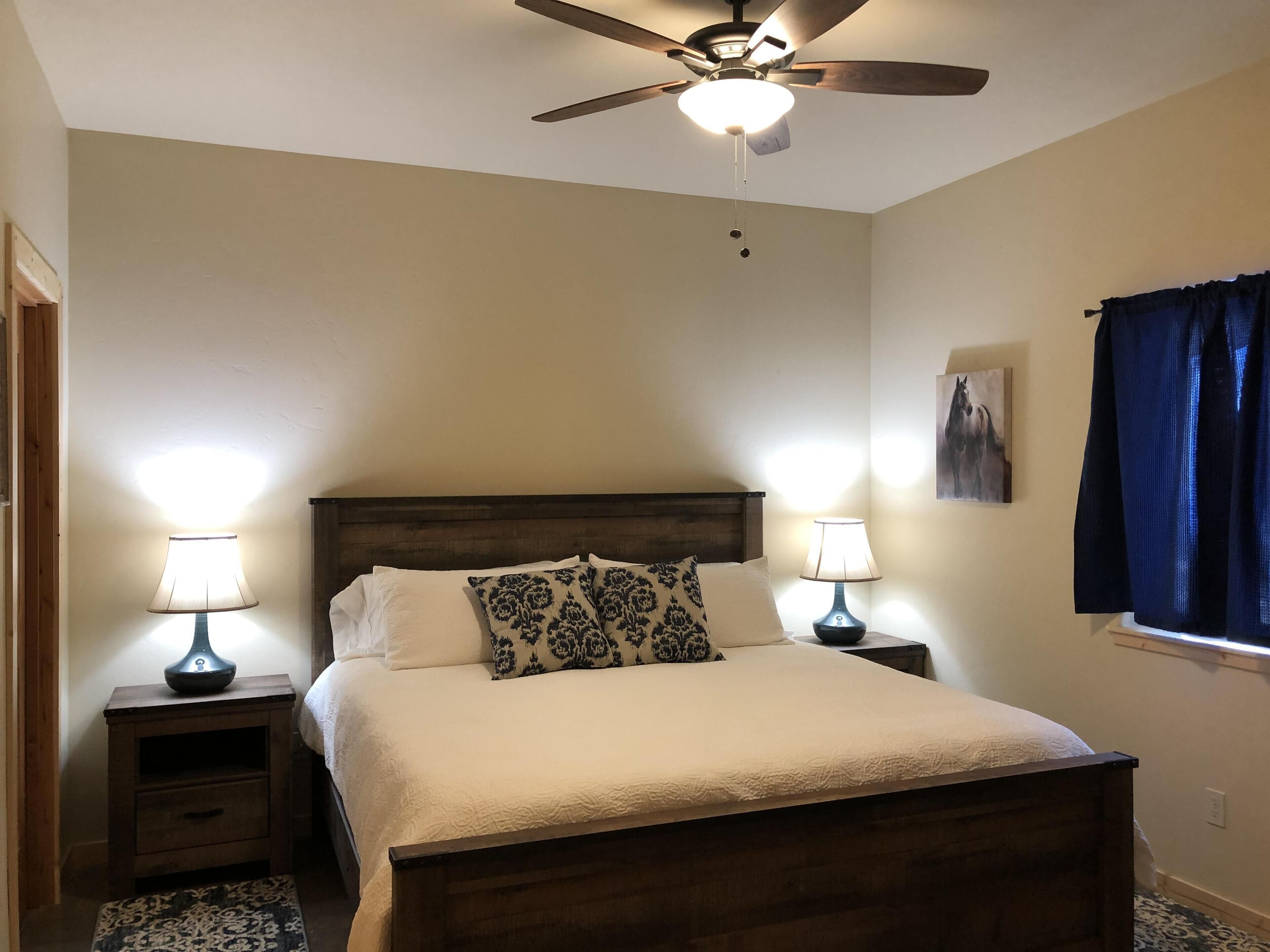 Une chambre à coucher avec un lit en bois, deux tables de chevet avec des lampes, un ventilateur de plafond et une fenêtre avec des rideaux.