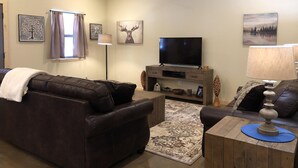 A living room with a brown leather sofa, a wooden coffee table, a TV on a wooden stand, and a floor lamp.