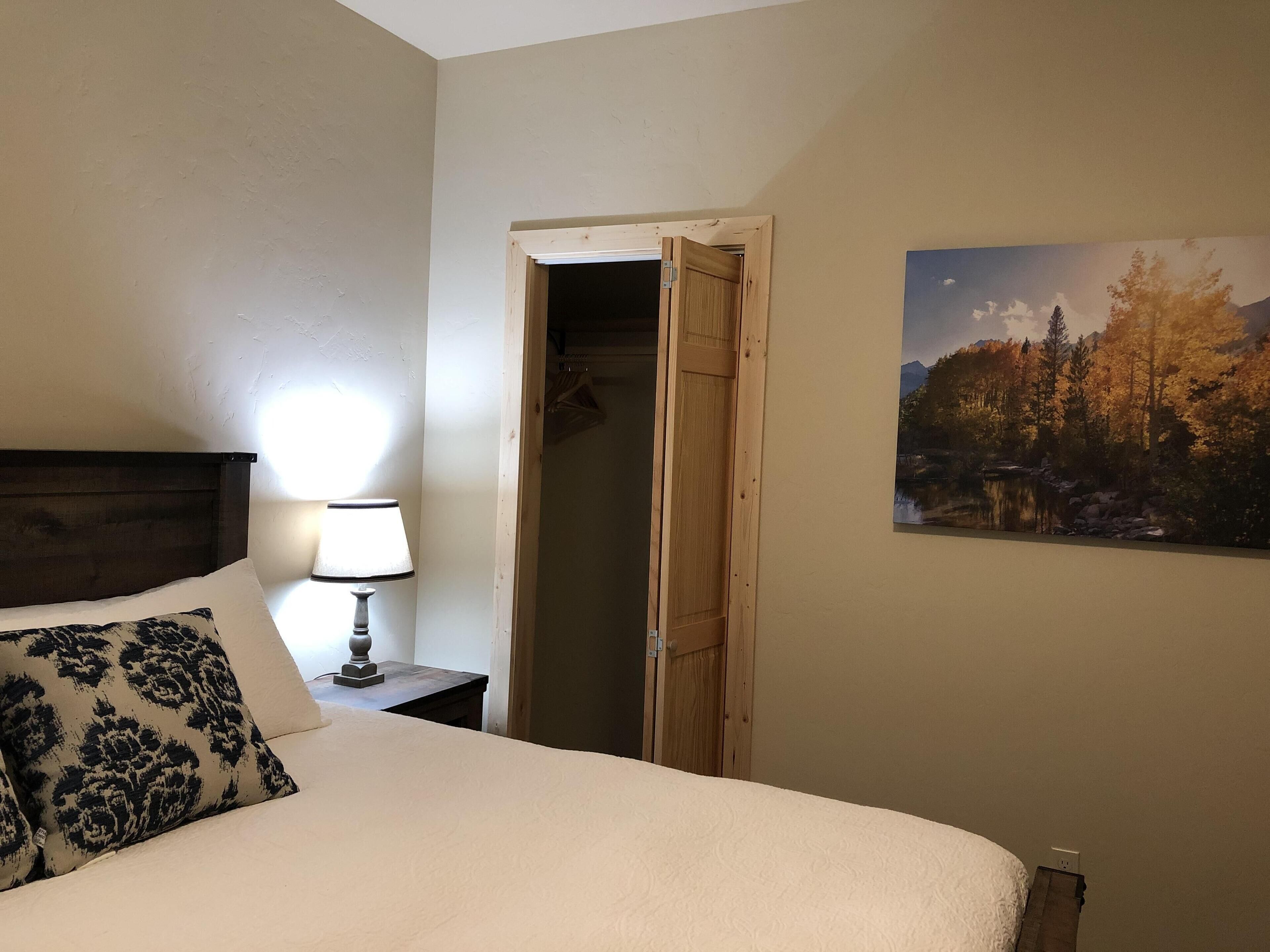 Une chambre d’hôtel avec un lit, une lampe de chevet, une porte en bois et un tableau représentant un paysage accroché au mur.