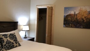 A hotel room with a bed, a bedside lamp, a wooden door, and a landscape painting on the wall.