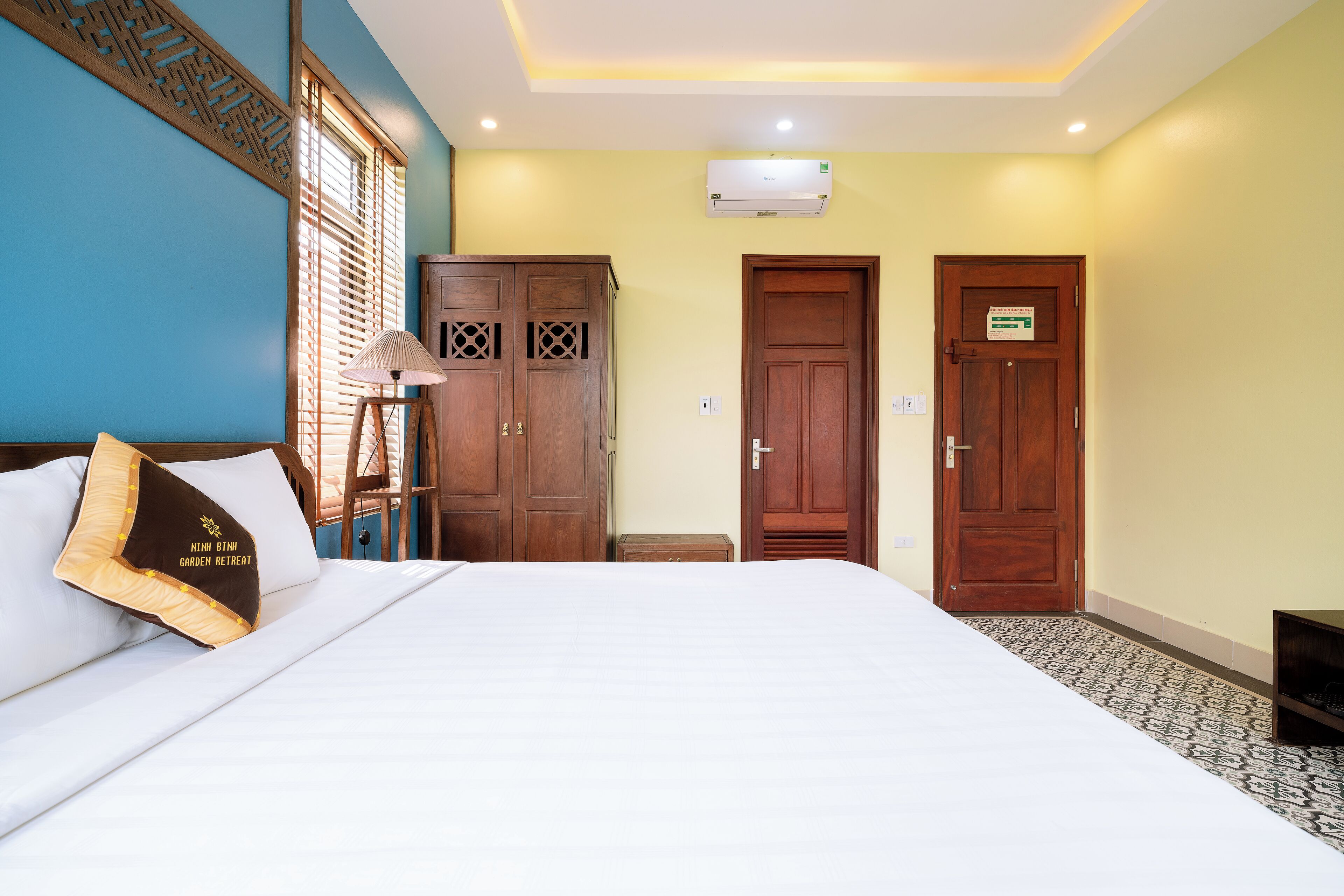 A hotel room with a bed, wooden wardrobe, and a door with a sign.