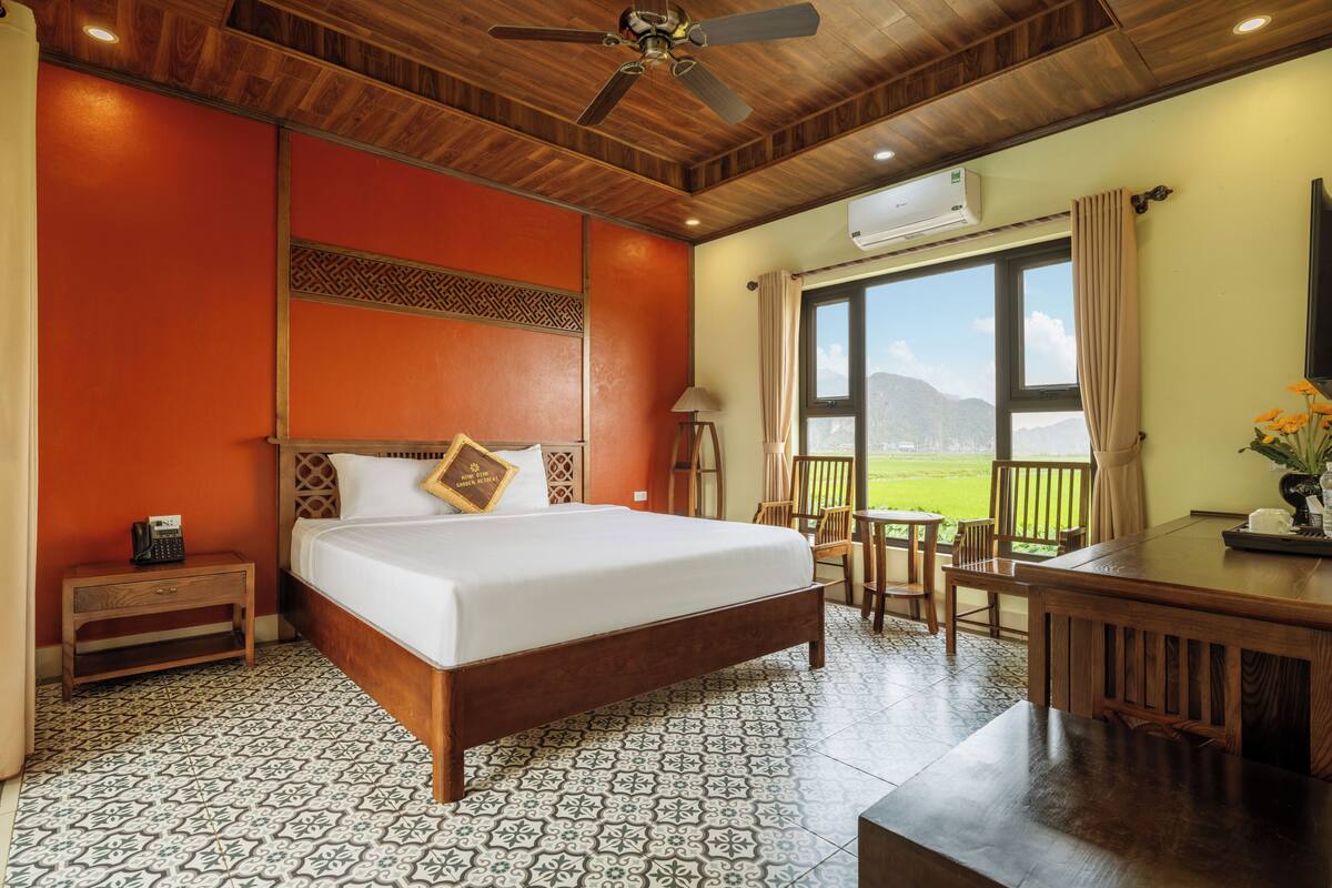 Quarto de hotel com uma cama grande, teto de madeira, escrivaninha com cadeiras e vista para o exterior.