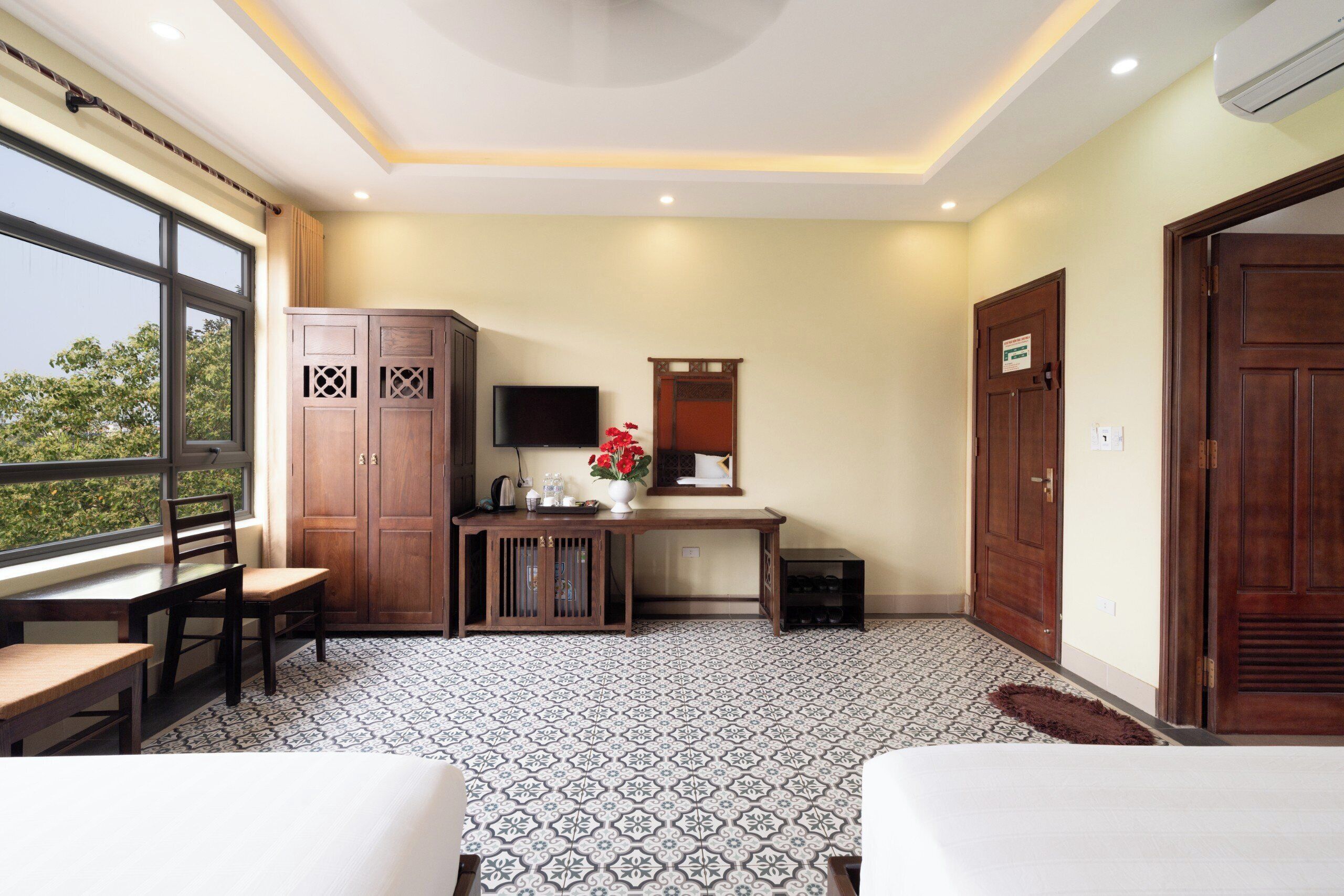 A hotel room with a large window, a desk with a flat-screen TV, a wooden cabinet, and two beds.