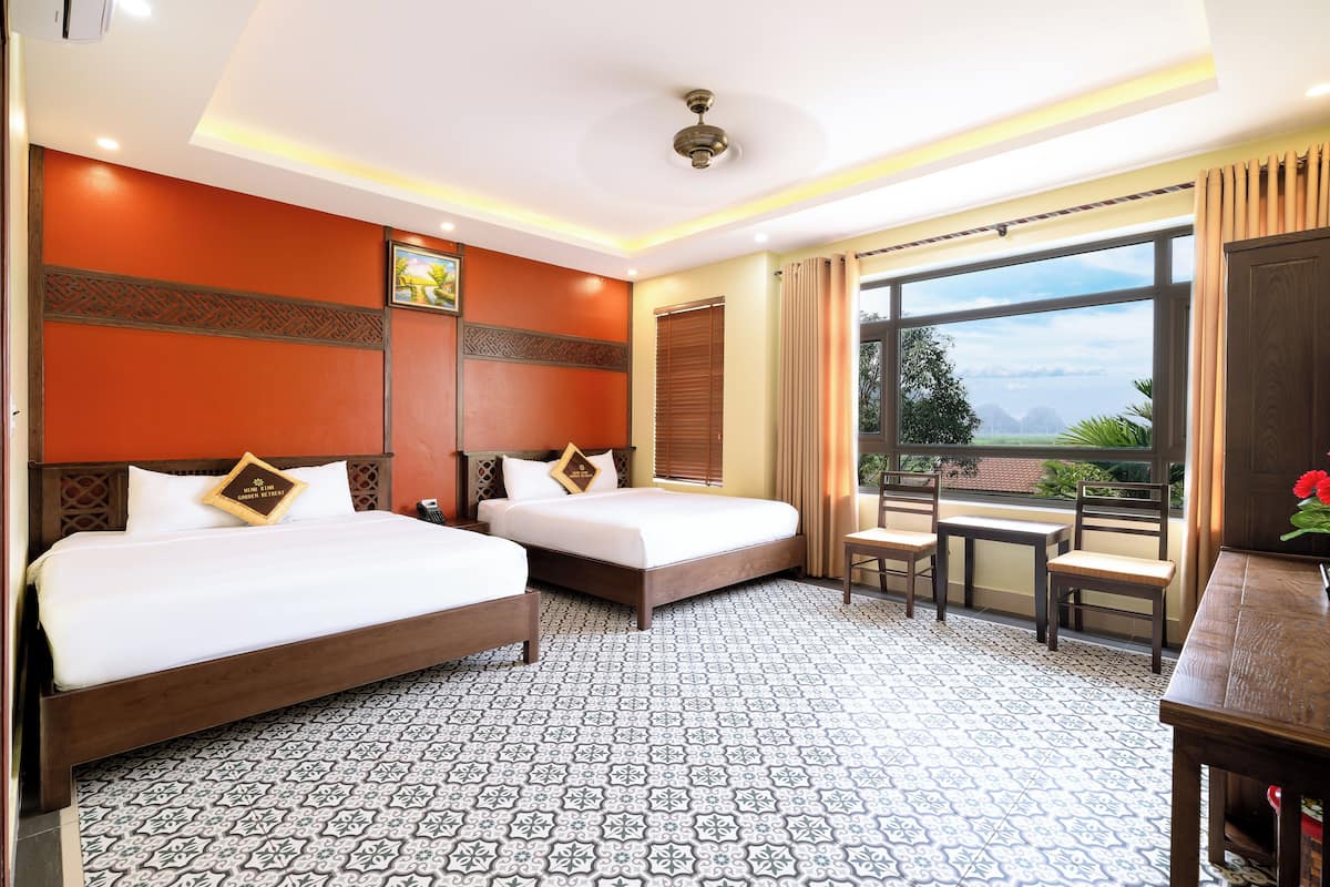 Quarto de hotel com duas camas, uma mesa pequena, janela com vista e piso de azulejos estampados.