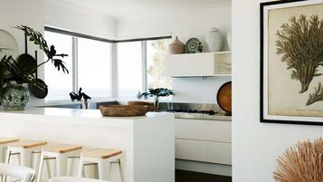 A modern kitchen with white cabinetry, a central island with stools, a large window, and various decorative items.