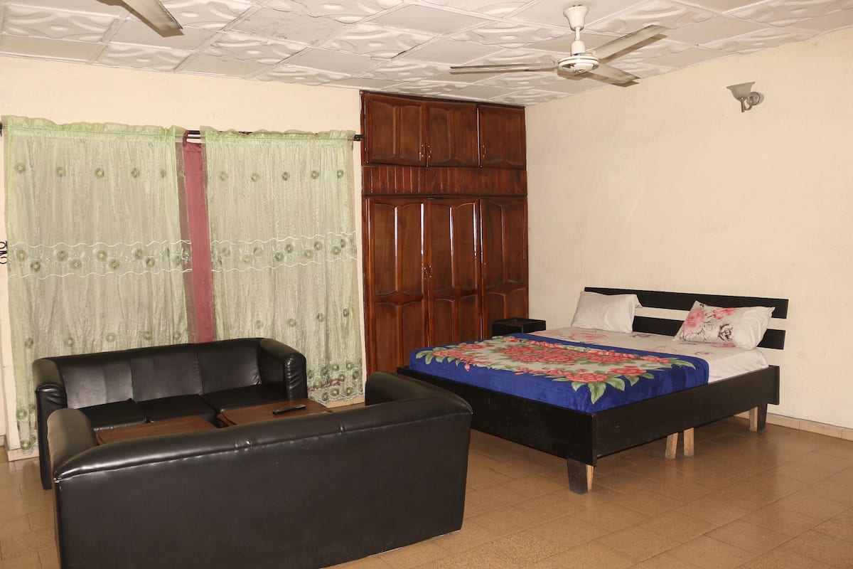 Un dormitorio con cama, sofá, armario y ventilador de techo.