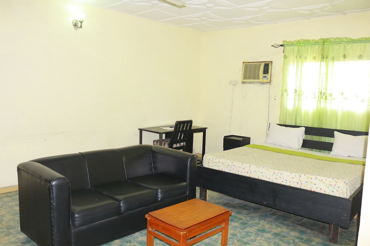 Una habitación con un sofá de cuero negro, una mesa de madera, una cama con cortina verde y un escritorio pequeño con una silla.