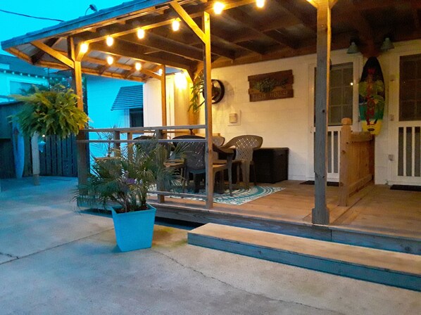 An outdoor covered patio area with string lights, a seating arrangement, and a potted plant.
