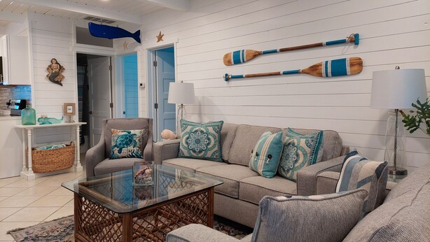 A living room with a glass coffee table, grey sofa with patterned cushions, a wicker side table, and a blue door in the background. - VINTAGE BEACH COTTAGE
BOOK NOW! SAVE!!
90 sec. walk to beach!
Supplies Included! (North Myrtle Beach)