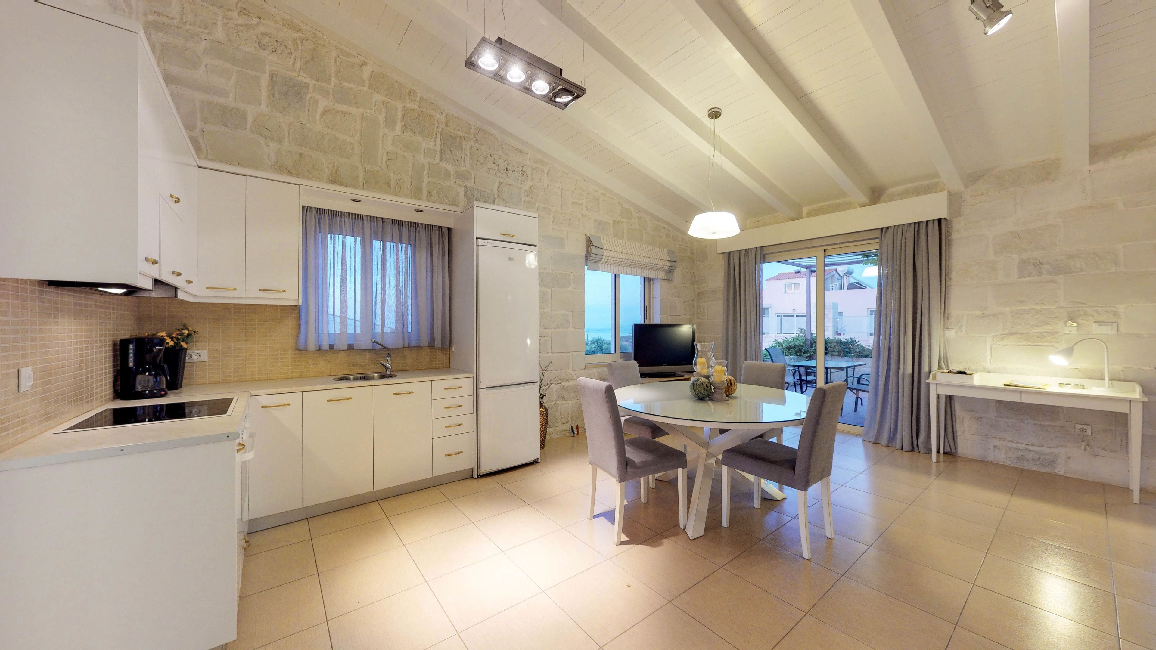 Une cuisine moderne avec des meubles blancs, un four encastré et un coin repas comprenant une table et des chaises en verre.