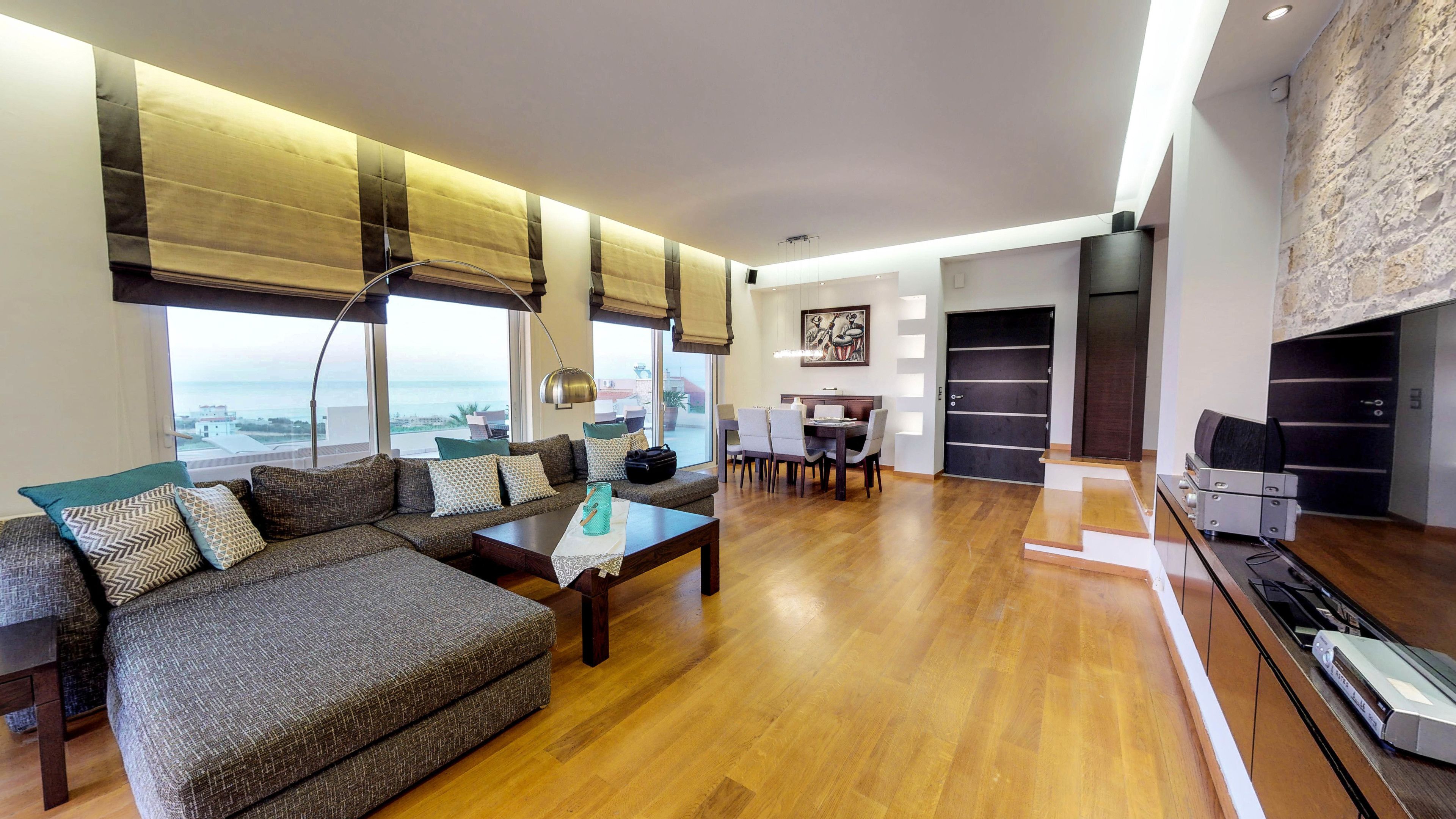 A modern living room with a sofa set, a dining area, and a kitchen.