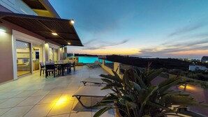A terrace with a pool, outdoor furniture, and a view of the coastline at dusk. - Lofos Village Chania (Chania)