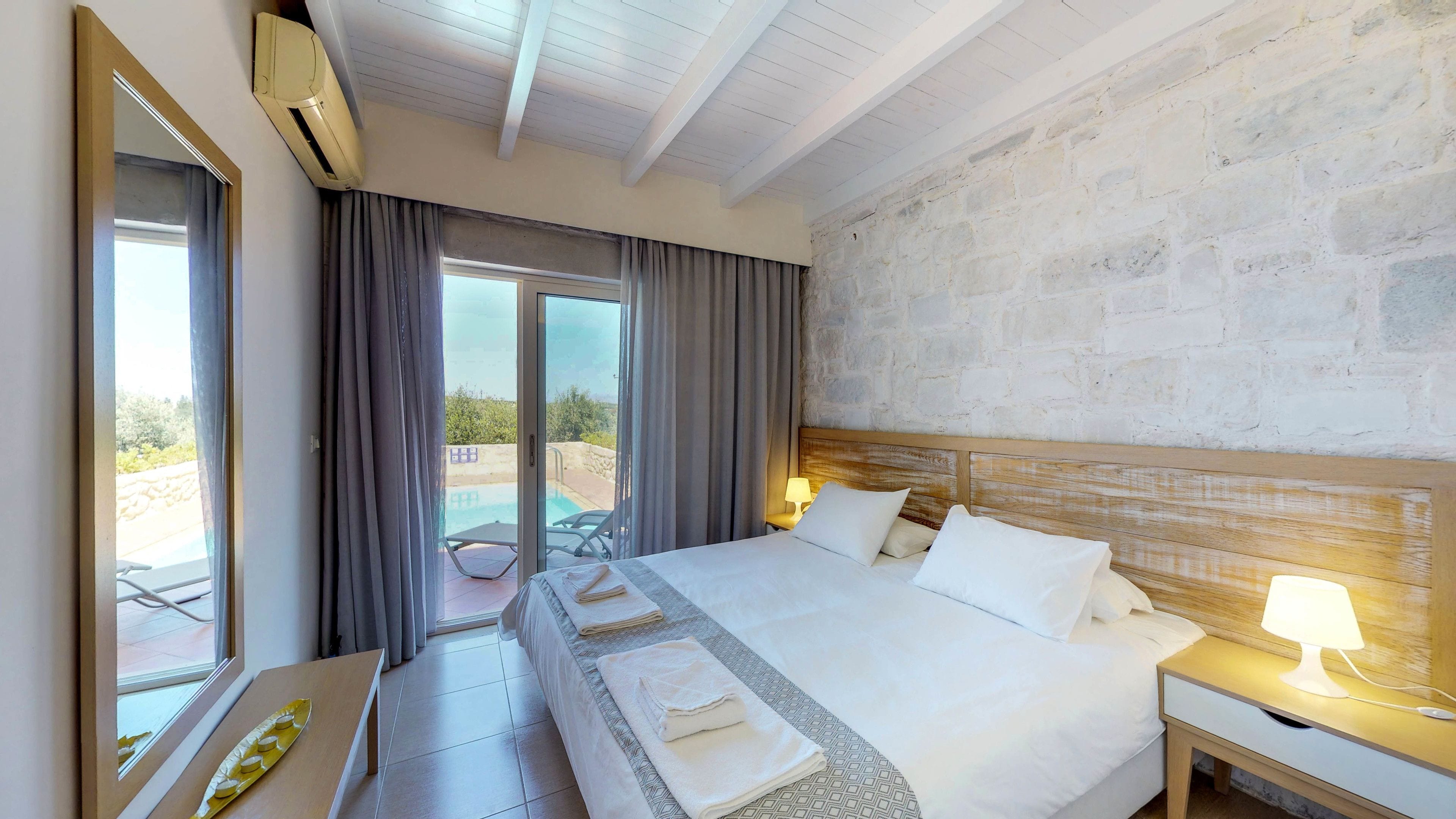 A hotel room with a large bed, a desk, a chair, a lamp, and a view of the outdoors.