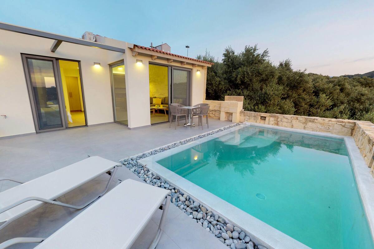 A modern outdoor pool area with a stone border, a dining set, and a building with sliding doors.