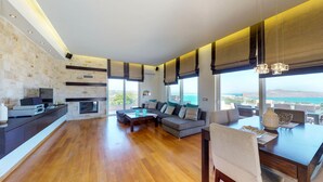 A spacious living area with a large sofa set, a dining table, and a kitchen area with a built-in TV. - Lofos Village Chania (Chania)