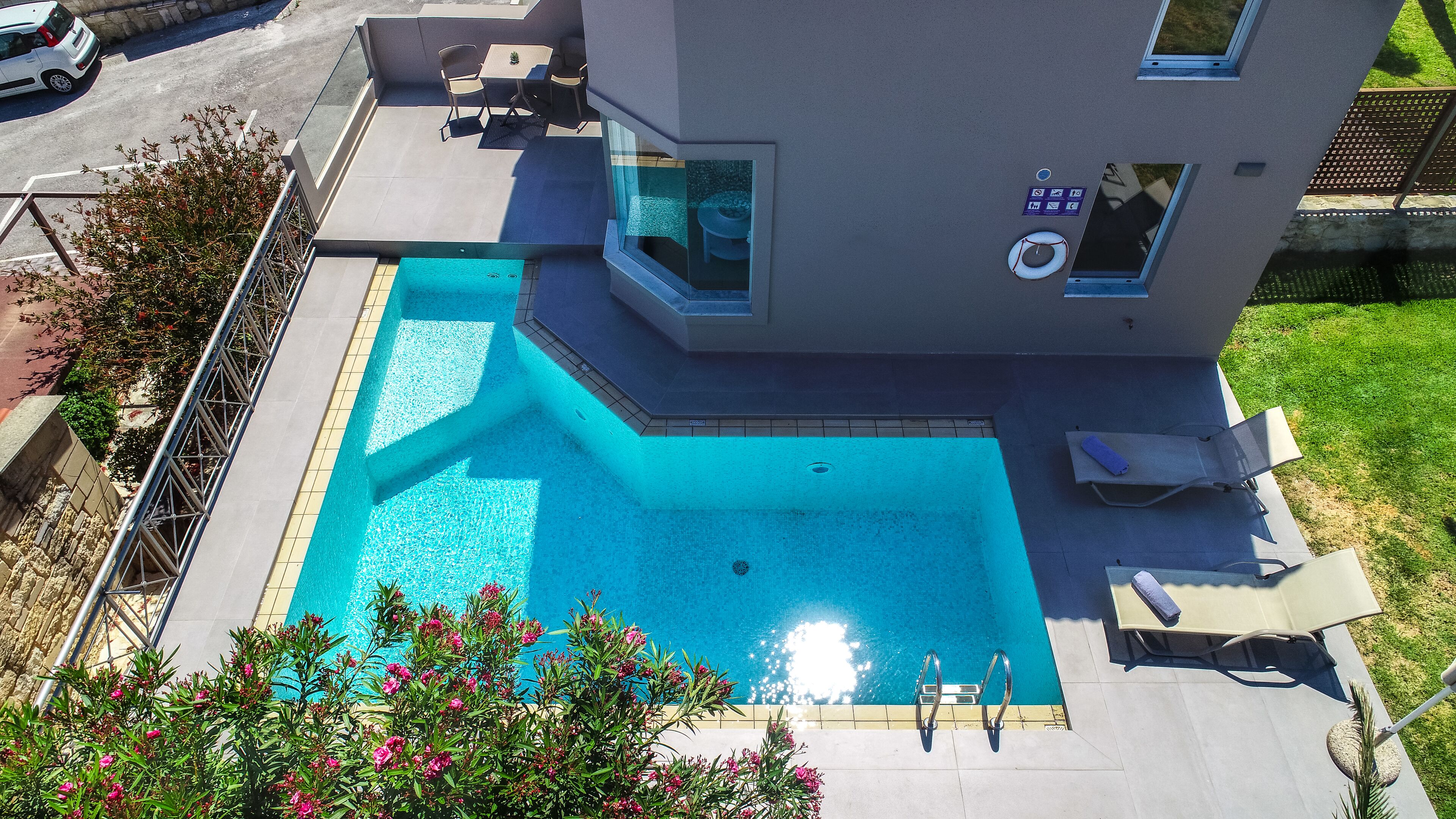A modern building with a swimming pool, outdoor seating, and a small garden area.