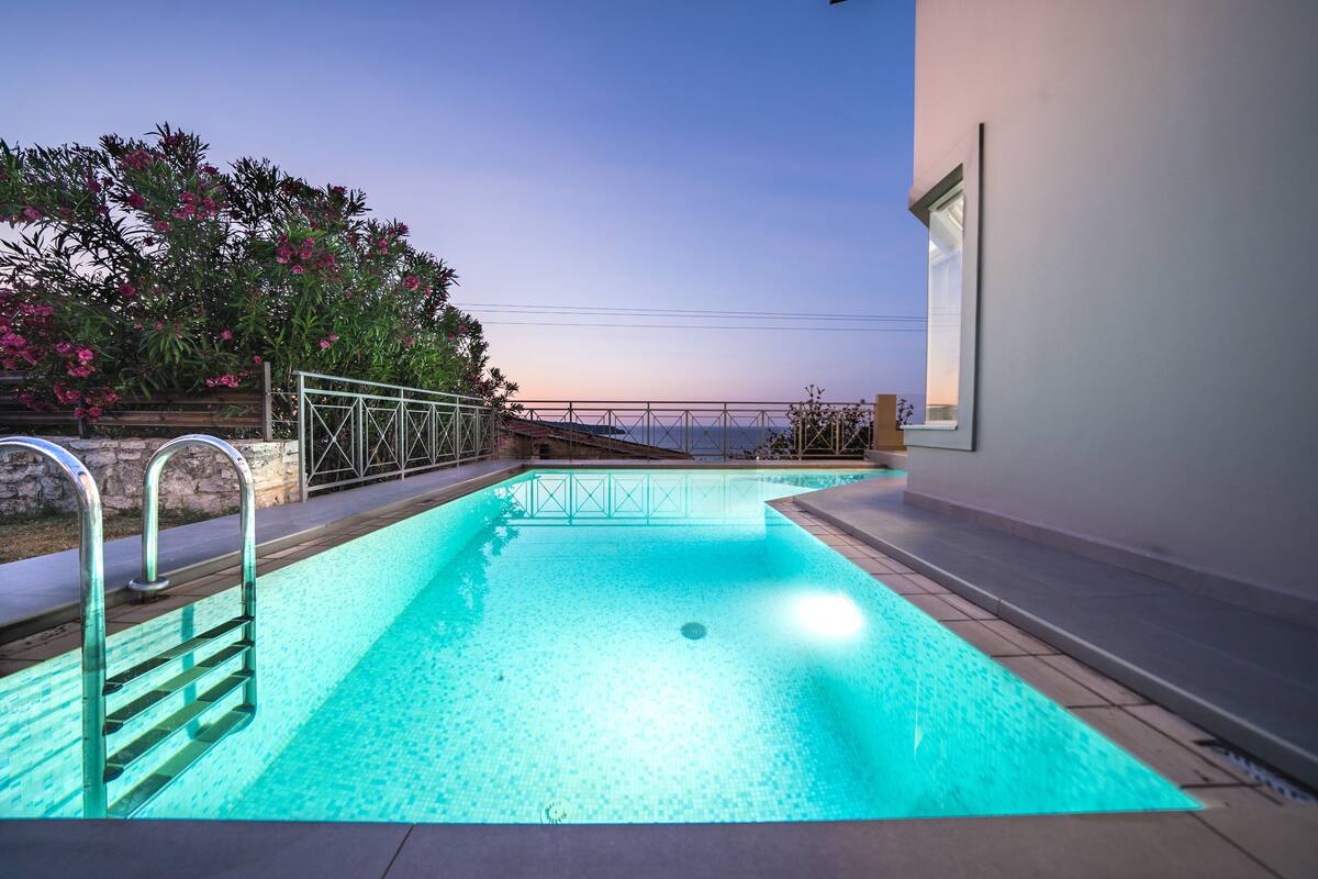 A swimming pool with a metal ladder, surrounded by a low wall and a railing.