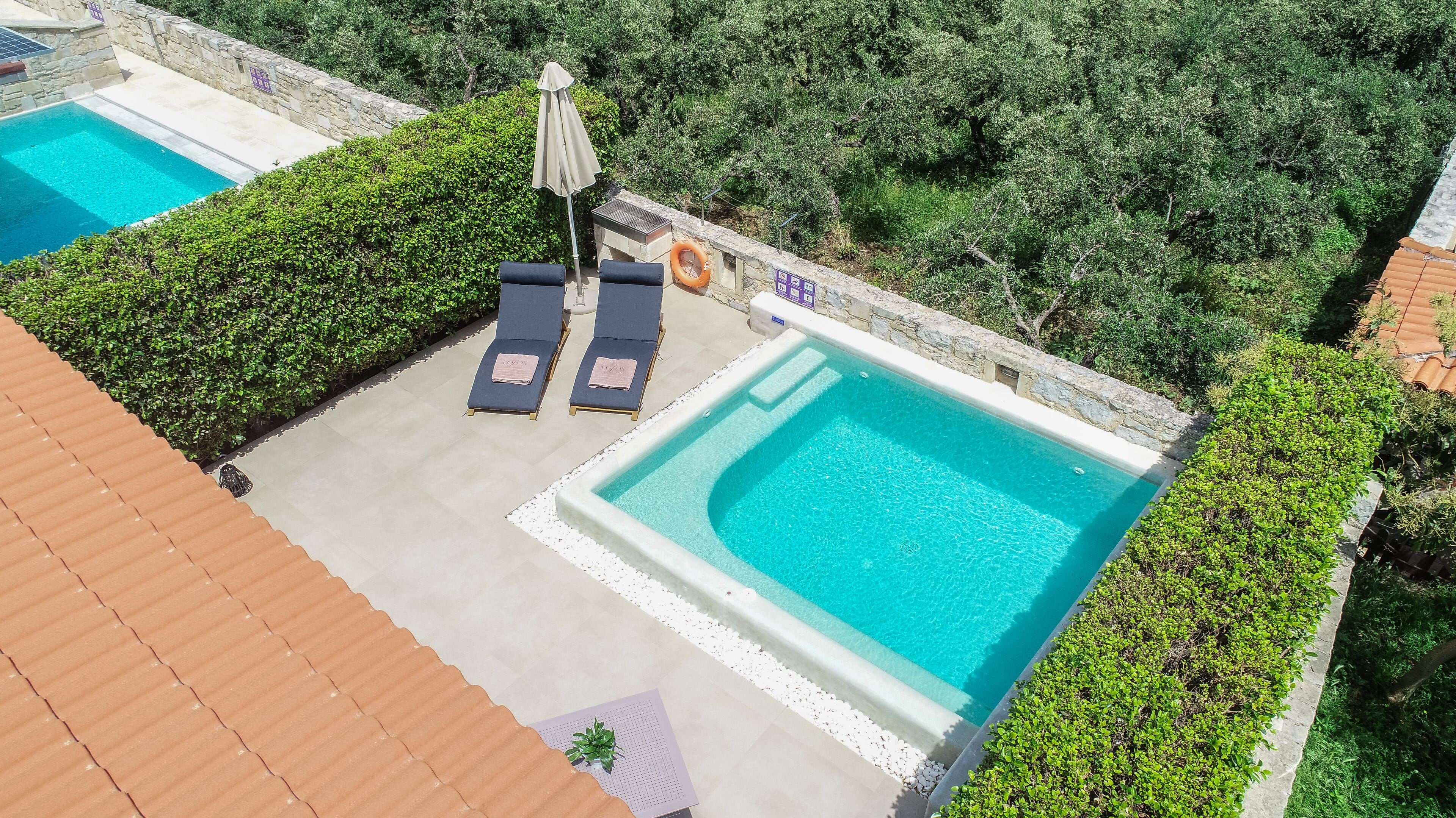 Un área de piscina en la azotea con dos sillones de descanso, una sombrilla y un flotador salvavidas.