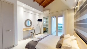 A modern bedroom with a bed, a desk, a chair, a TV, and a balcony with a view. - Lofos Village Chania (Chania)