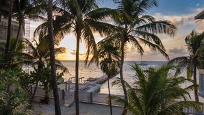 Blick auf einen Strand mit Palmen, einem Steg und einem Sonnenuntergang.