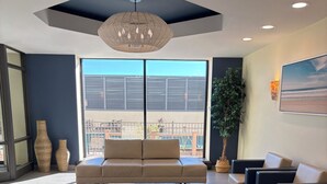A modern living room with a large sectional sofa, a hanging light fixture, and a view of the outdoors through large windows. - Luxury Oceanfront Condo  (Long Beach)