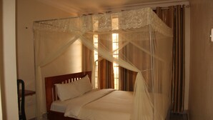 Una cama con dosel, una silla y una ventana con cortinas.