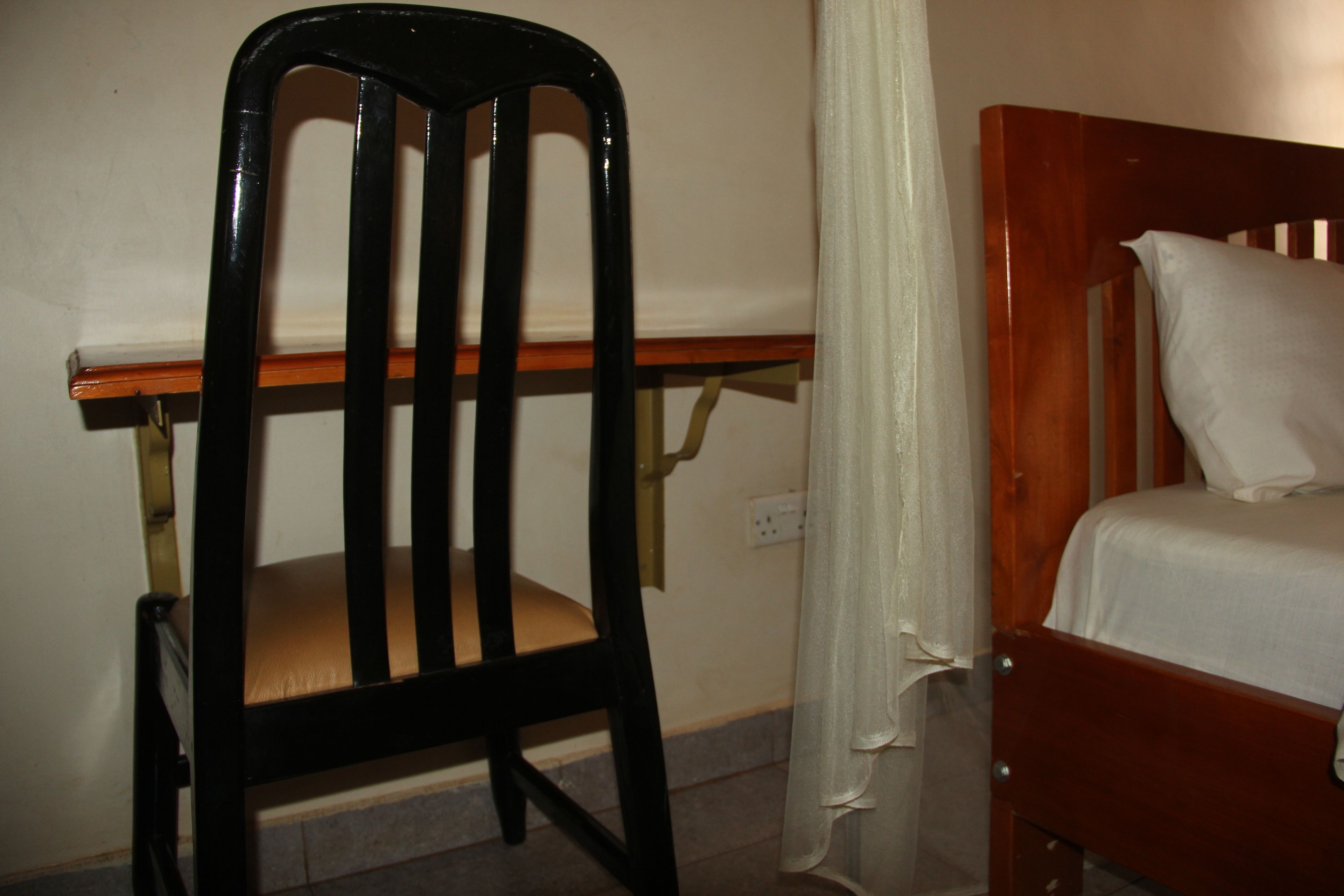 A simple room with a wooden chair, a small wooden table, and a bed with a white mattress and pillow.