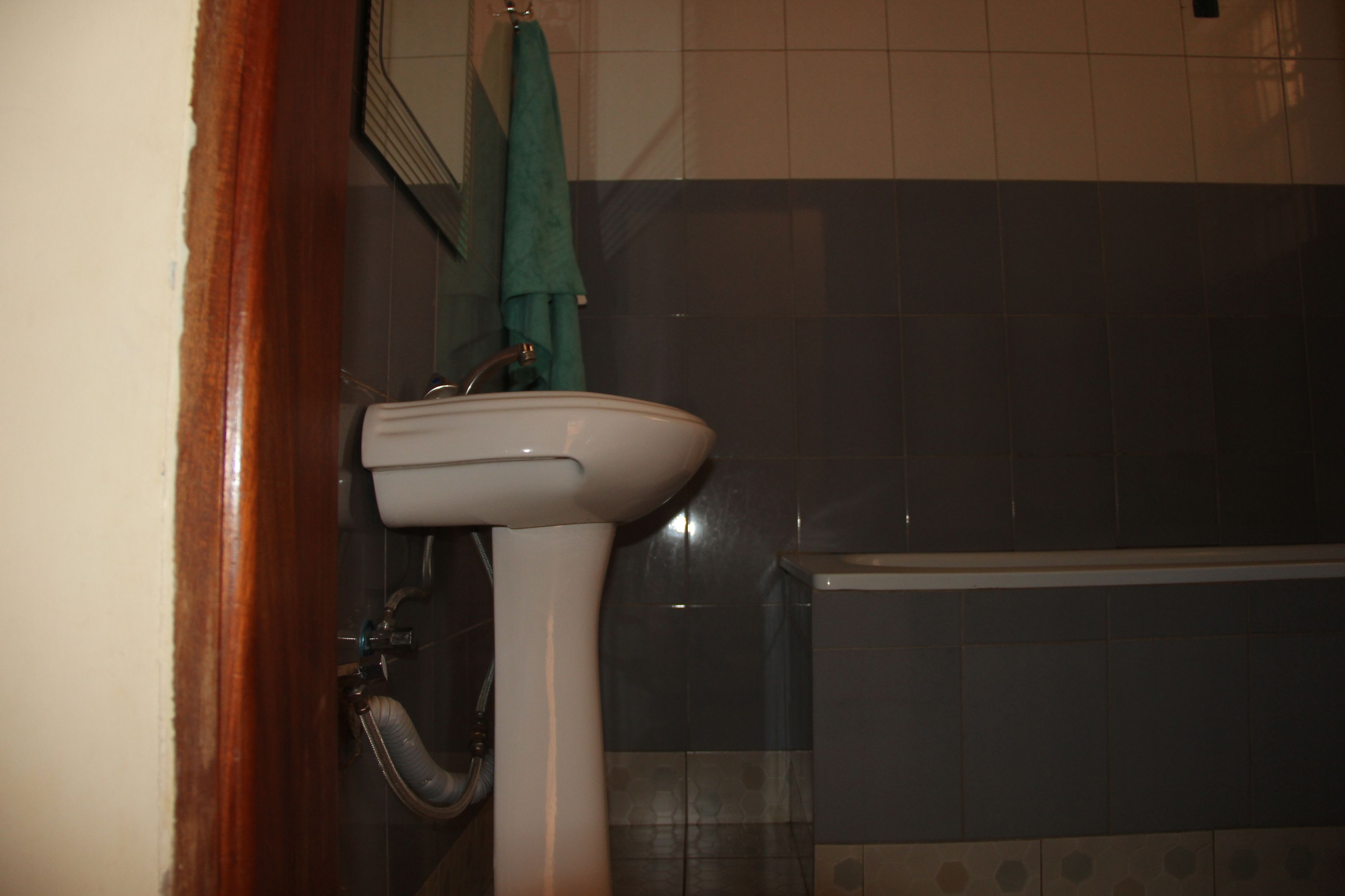 A bathroom with a white sink, a green towel hanging on the wall, and a bathtub.