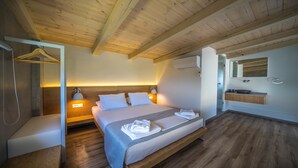 Un dormitorio moderno con techo de madera, cama con ropa de cama blanca, mesita de noche con lámpara y baño con espejo y lavabo.