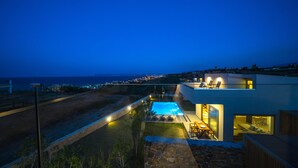 Una casa moderna con piscina, mobiliario exterior y vistas al mar al atardecer.