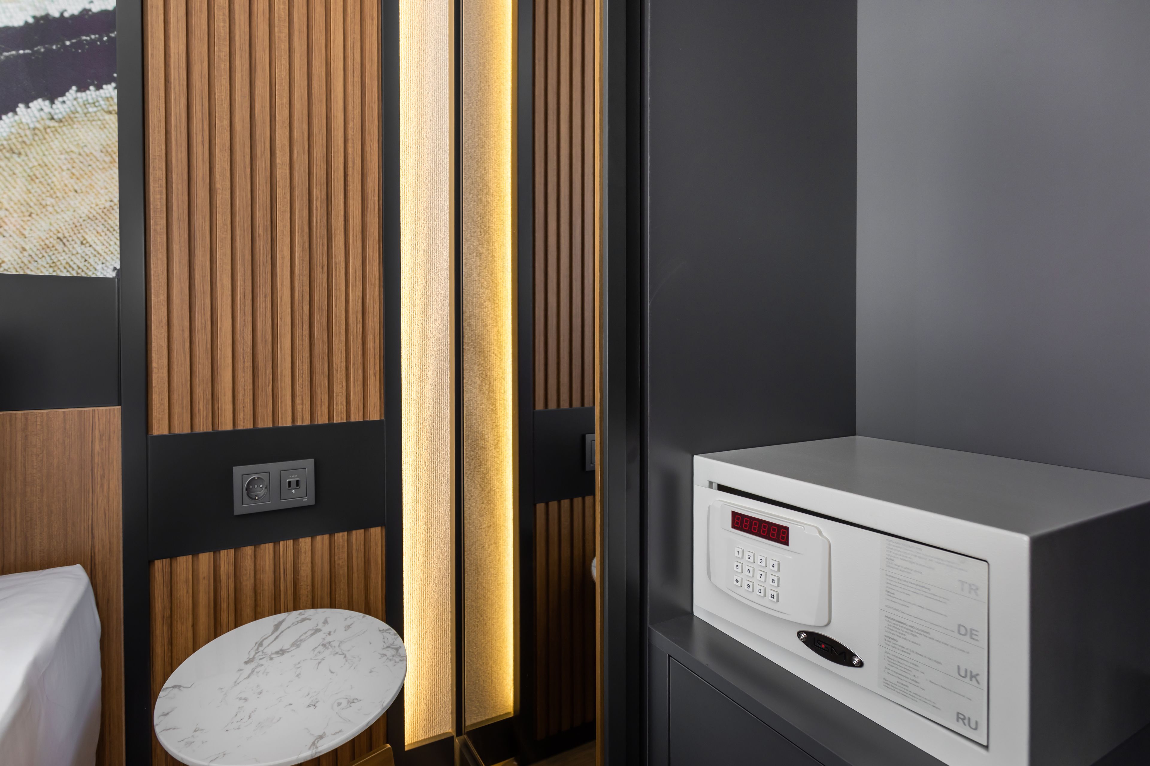 A modern hotel room with a wooden panel wall, a marble-topped table, and a digital control panel.