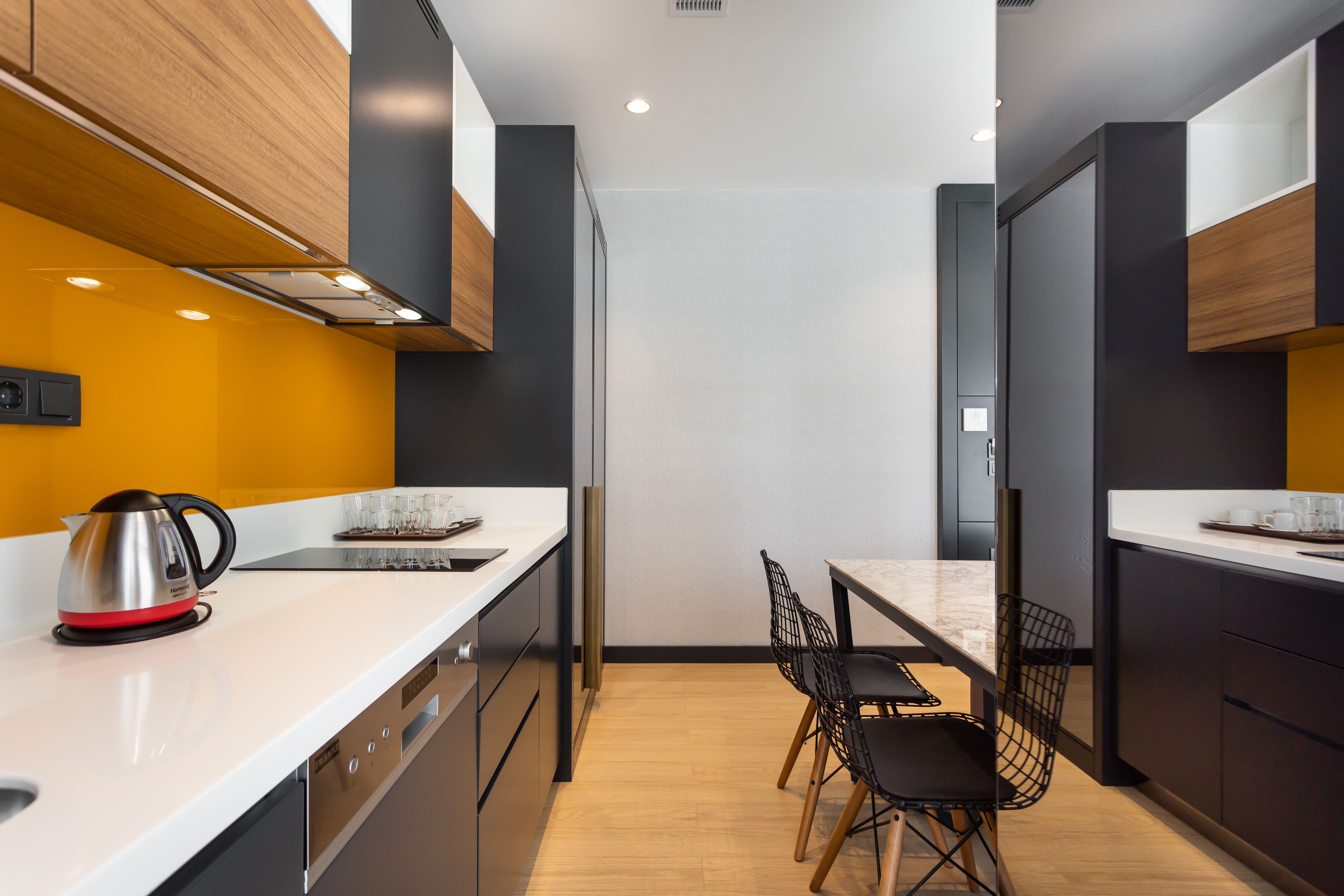 A modern kitchen with wooden cabinets, a white countertop, and a dining area with a table and chairs.