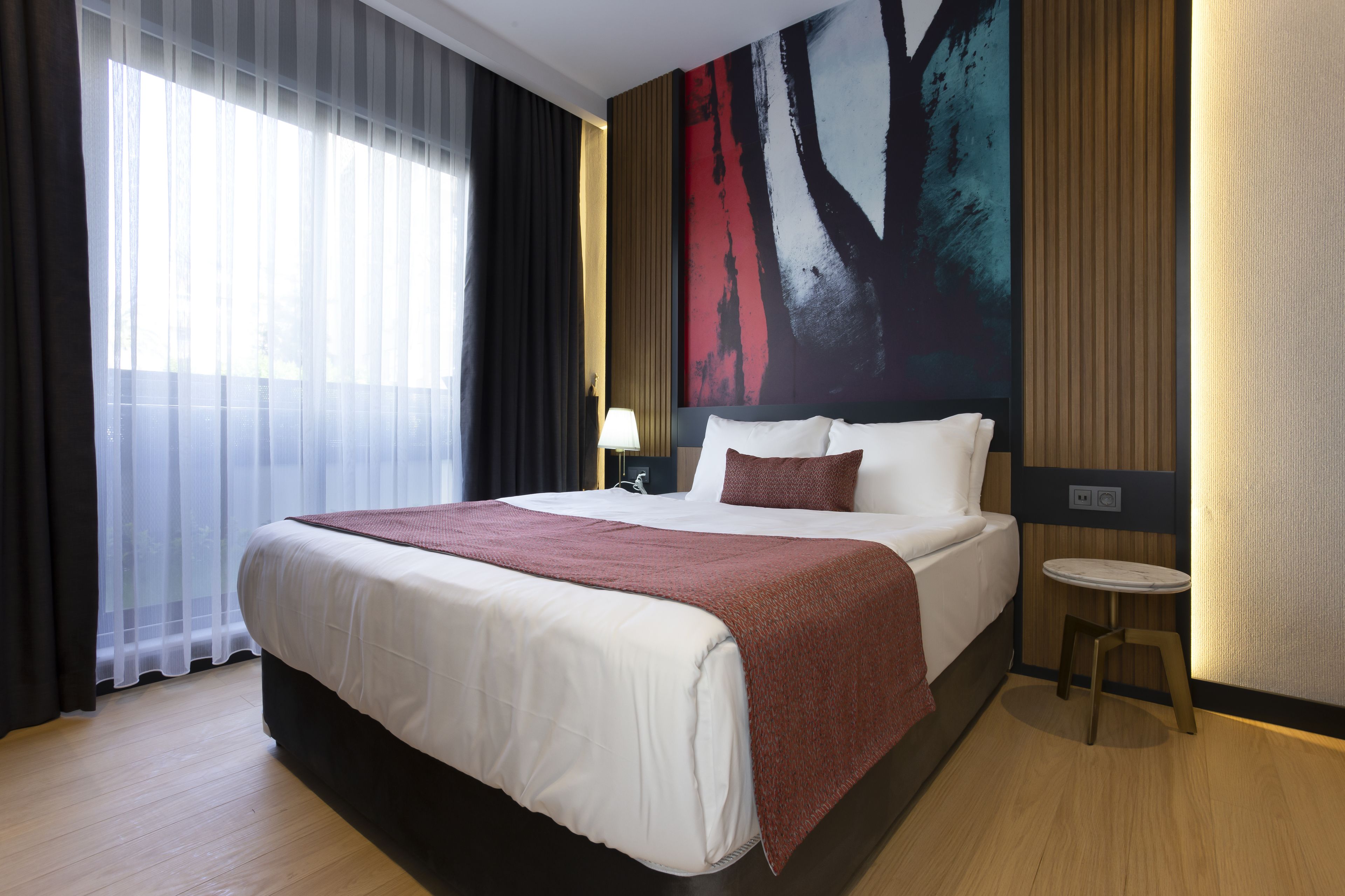 A hotel room with a large bed, a small round table, and a large abstract painting on the wall.
