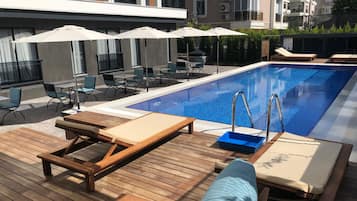 Un área de piscina con sillones reclinables, sombrillas y una terraza de madera.