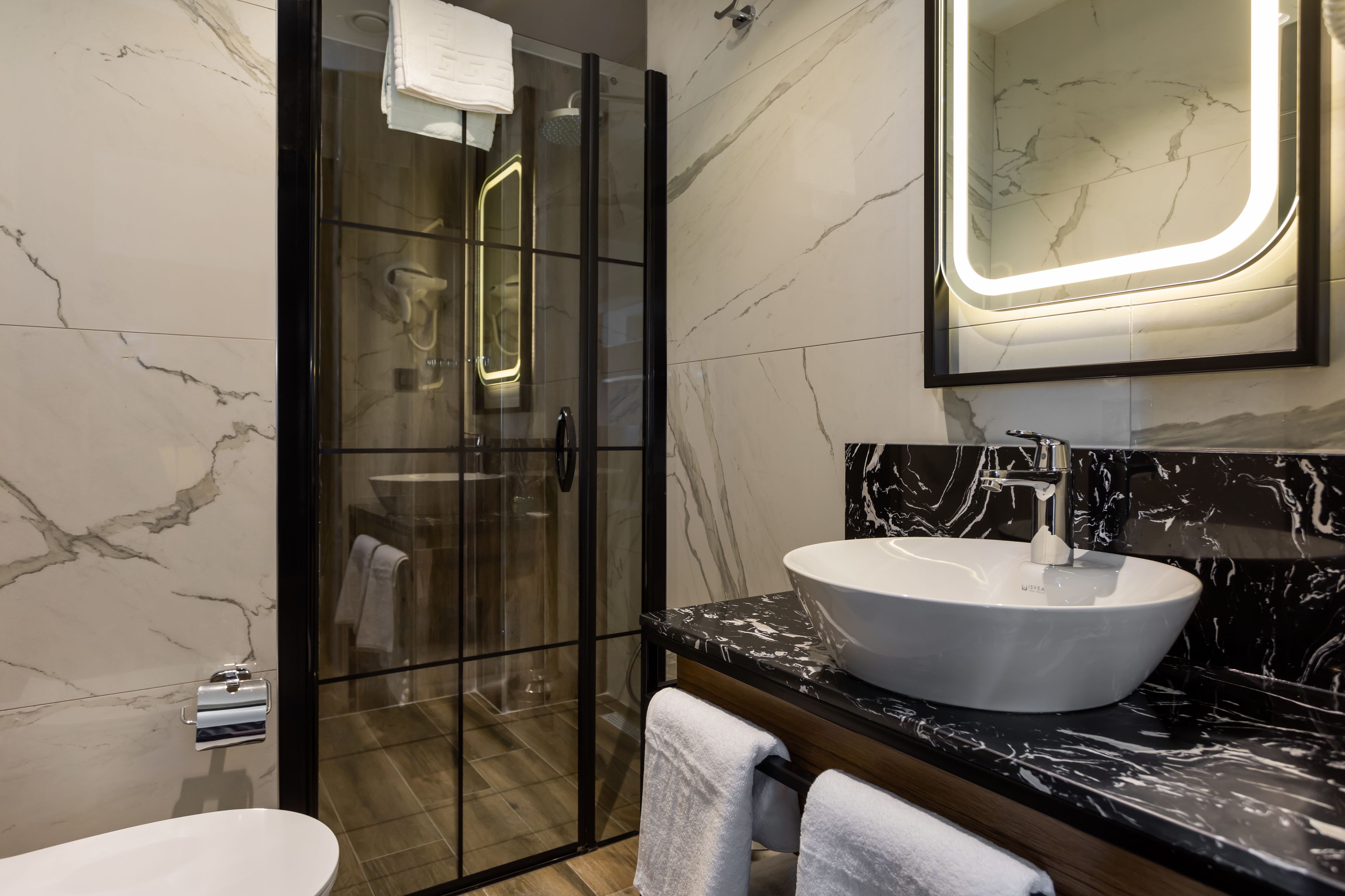 A modern bathroom with a glass-enclosed shower, a white sink, and a marble-tiled wall.