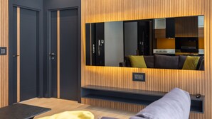 A modern room with dark walls, a wooden accent wall, a large mirror, a sofa, and a small table. - Nox Suite (Antalya)